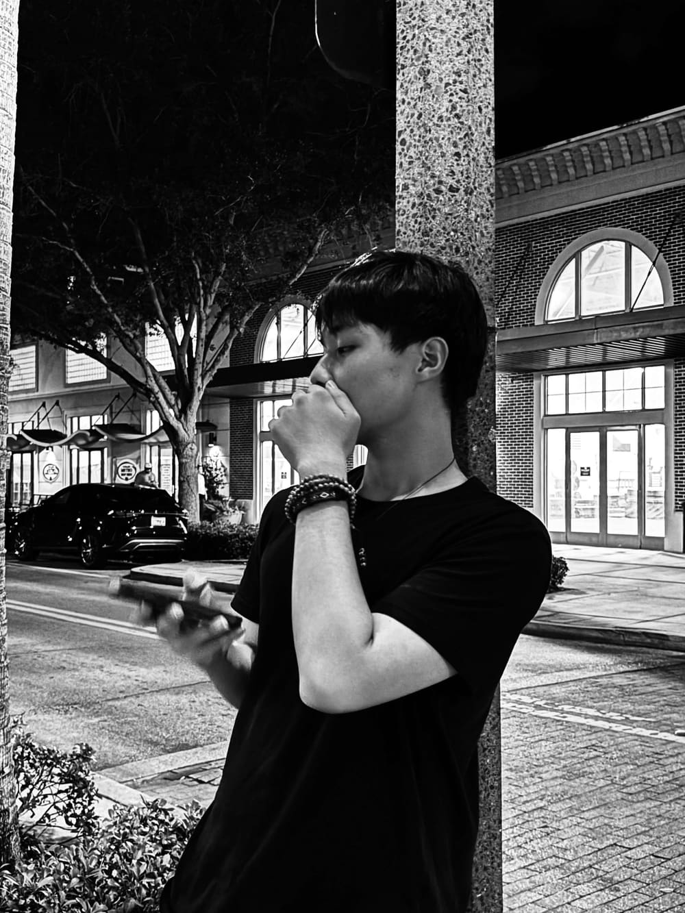 Black-and-white portrait of Long Nguyen standing beside a stone column at night.